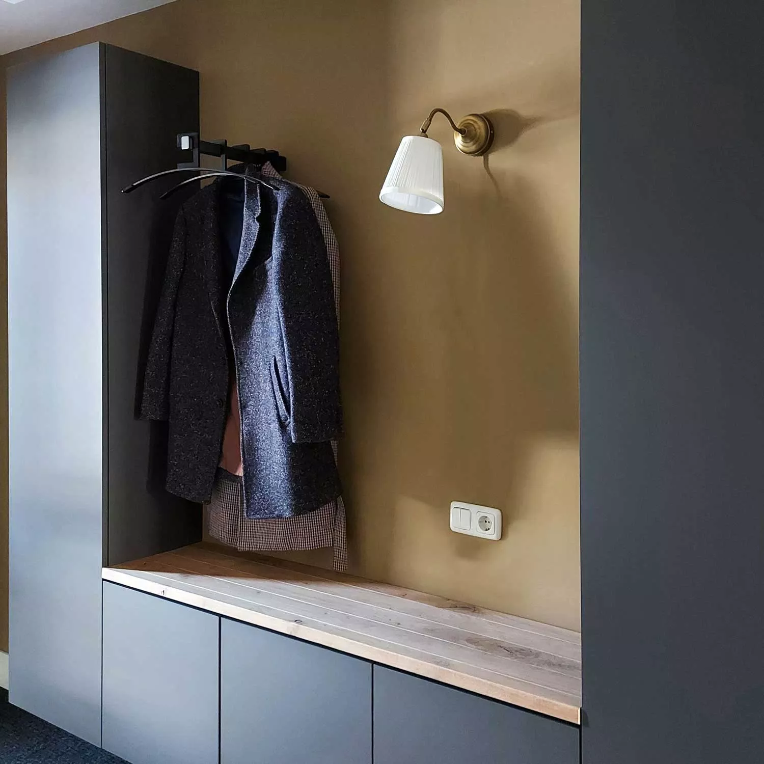 Wandgarderobe Imora quadratisch schwarz in einer Garderobennische mit Mänteln auf Kleiderbügeln montiert.