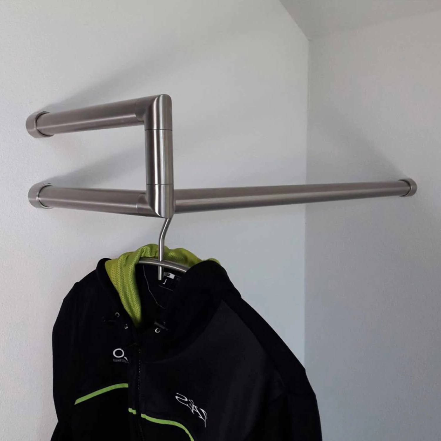 Wandgarderobe Lorien rund Edelstahl rechte Ecke in einer Garderobennische mit Mänteln auf Kleiderbügeln montiert.