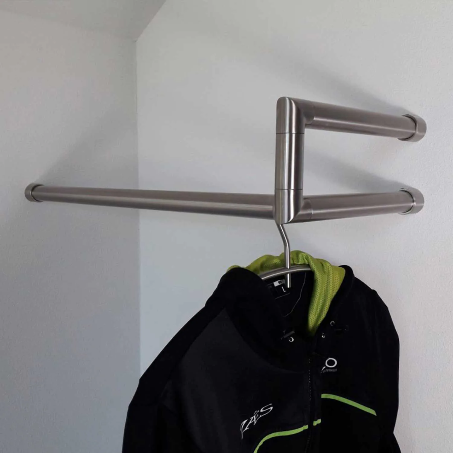 Wall-mounted coat rack Lorien round stainless steel left corner mounted in a wardrobe niche with coats on hangers.