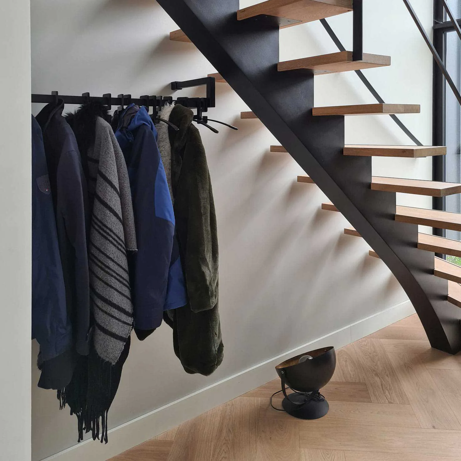 Schwarzer Edelstahl-Garderobenständer an der Treppe mit Kleiderbügeln und Mänteln